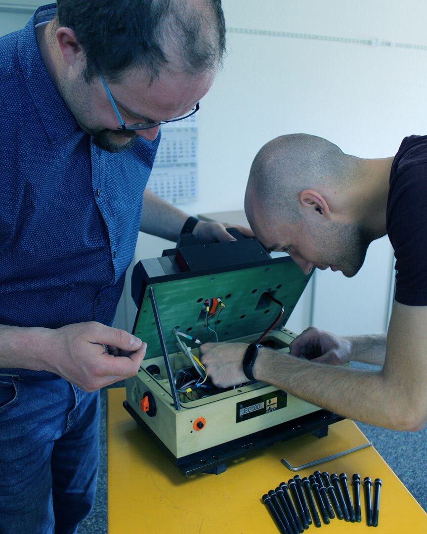 Zwei Personen arbeiten an einem kleinen Spannsystem.