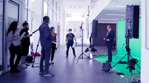 Eine Person vor einem Greenscreen und mehrere Personen hinter der Kamera.