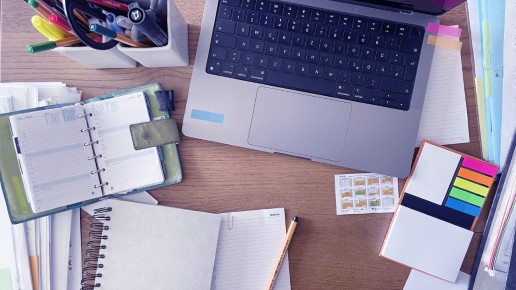 Ausschnitt eines Schreibtischs mit Planer, Laptop Stiften und Klebenotizen.