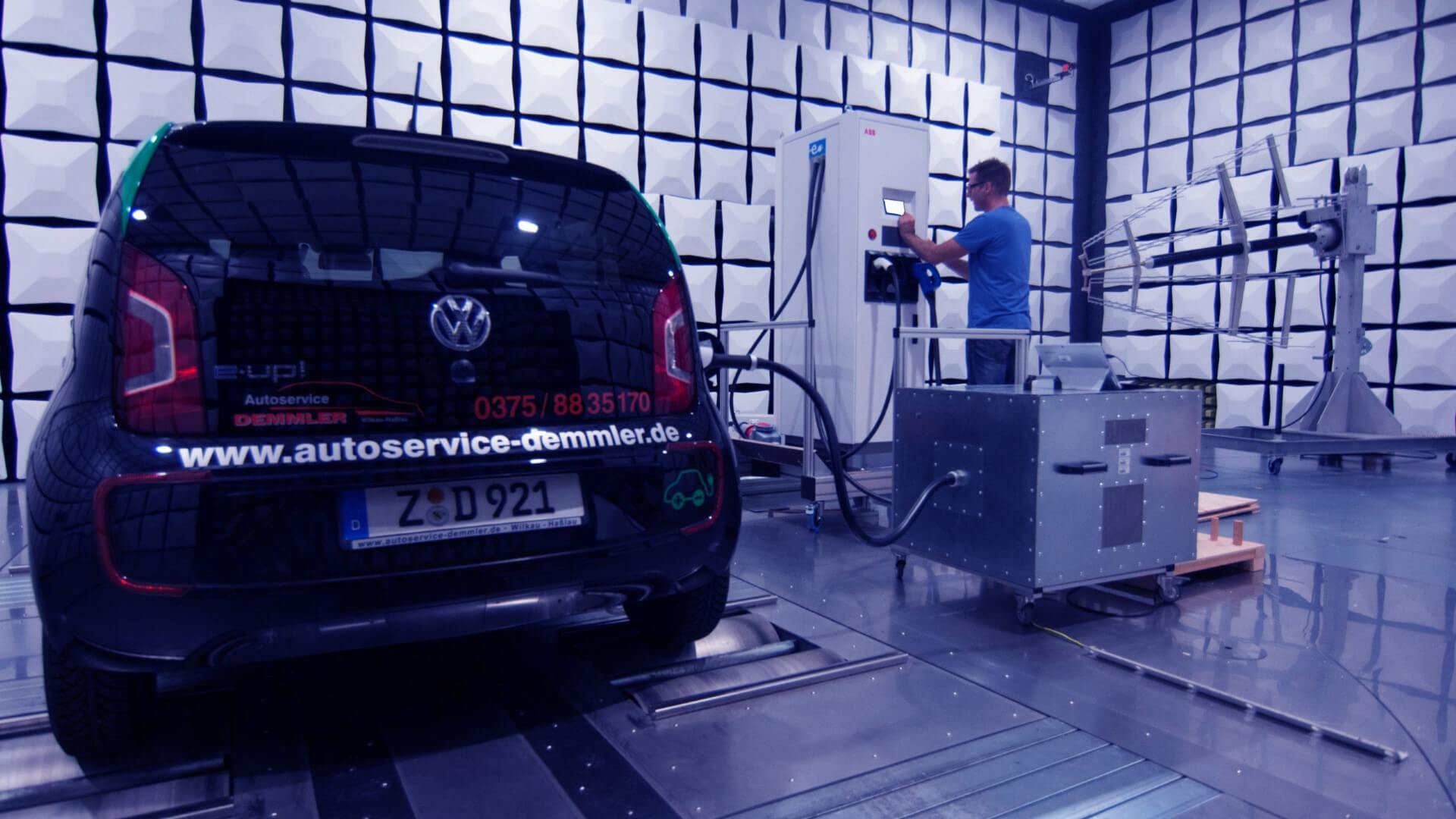 Auto auf einem Versuchsstand und eine Person die eine Ladesäule bedient.