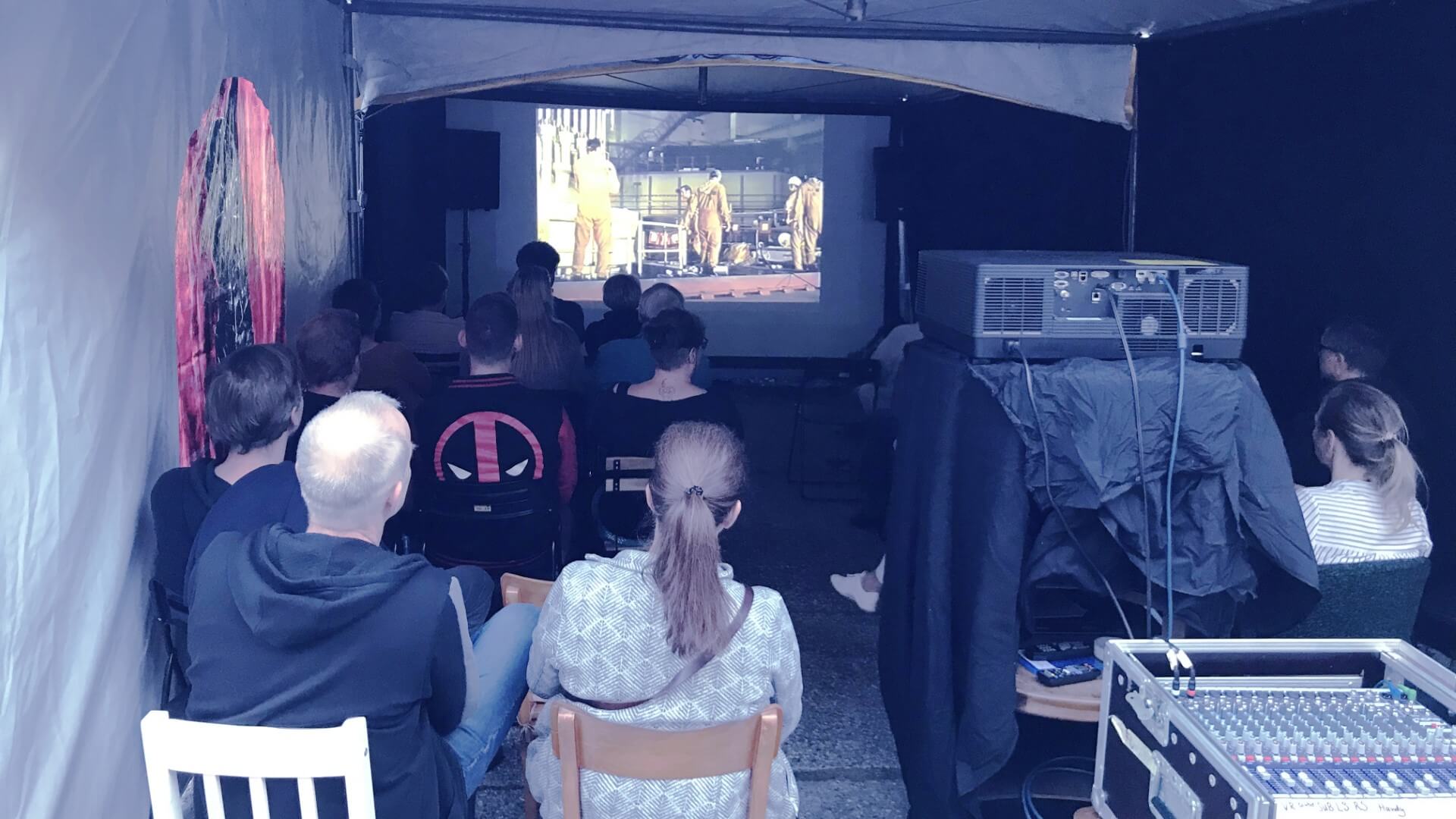 Blick von hinten auf die Leinwand in einem provisorischen Kinozelt mit Zuschauenden.